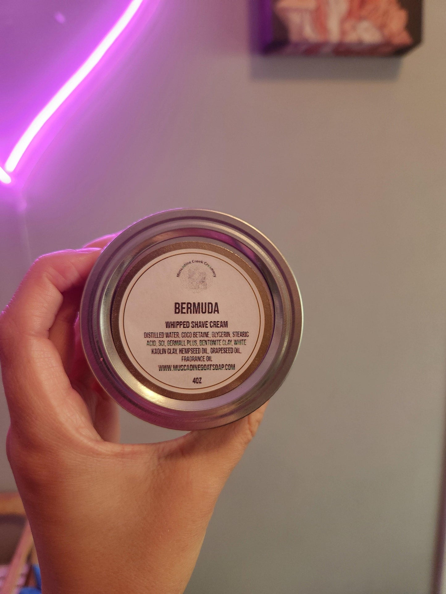 Hand holding a jar labeled 'Bermuda' with a purple neon light in the background.